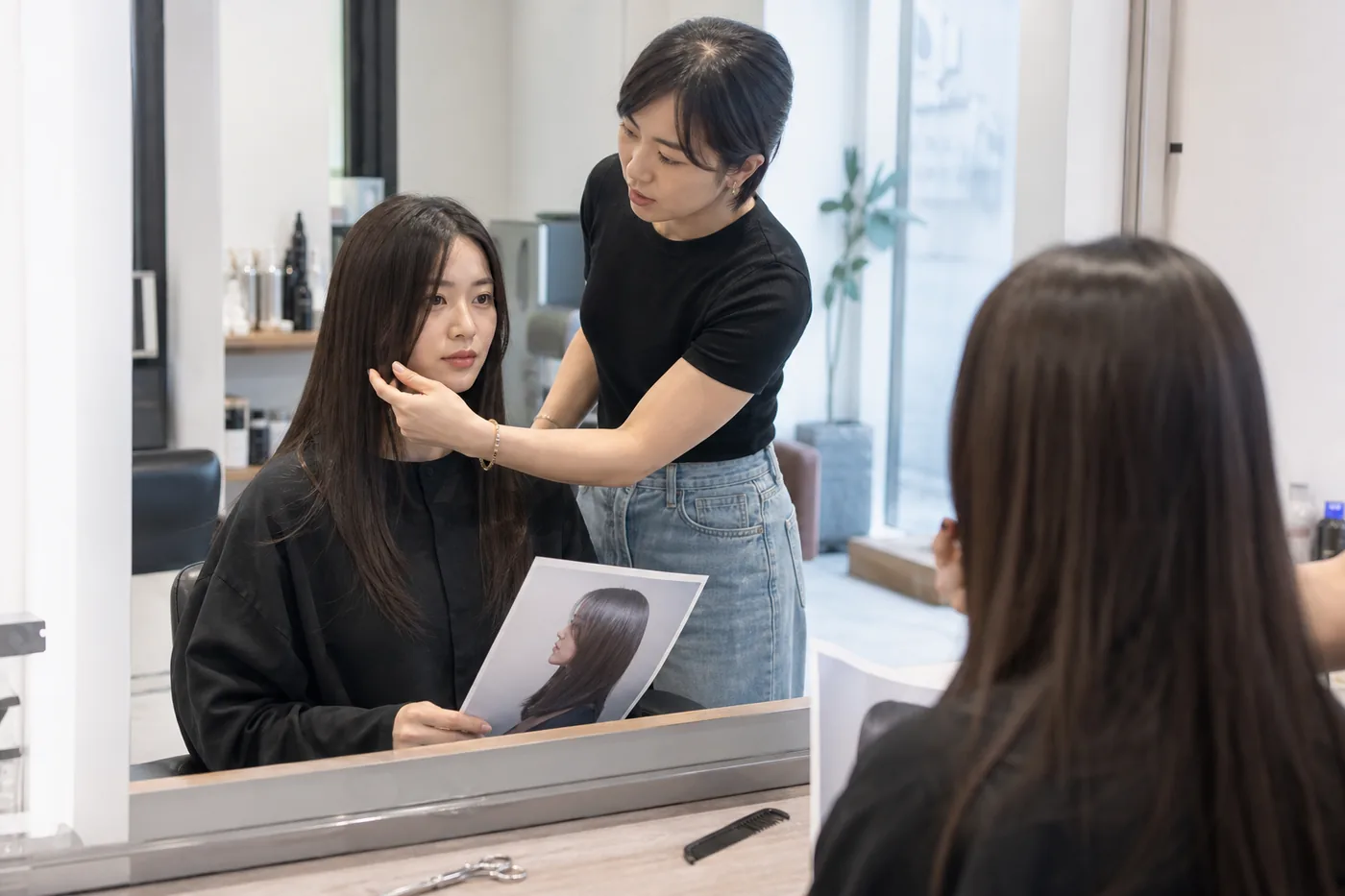 Stylist and client reviewing straight hair length and a reference photo before cutting